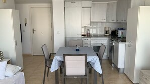 A compact kitchen with white cabinets, a dining table with chairs, and a small refrigerator.