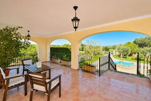 A covered patio with a table and chairs, a view of a garden with a fountain, and a clear sky. - Calderitx 253 fantastic finca with private pool, children's playground, barbecue and terrace (Ariany)