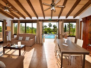 A spacious living area with a pool, wooden ceiling beams, and large windows offering a view of the outdoors.