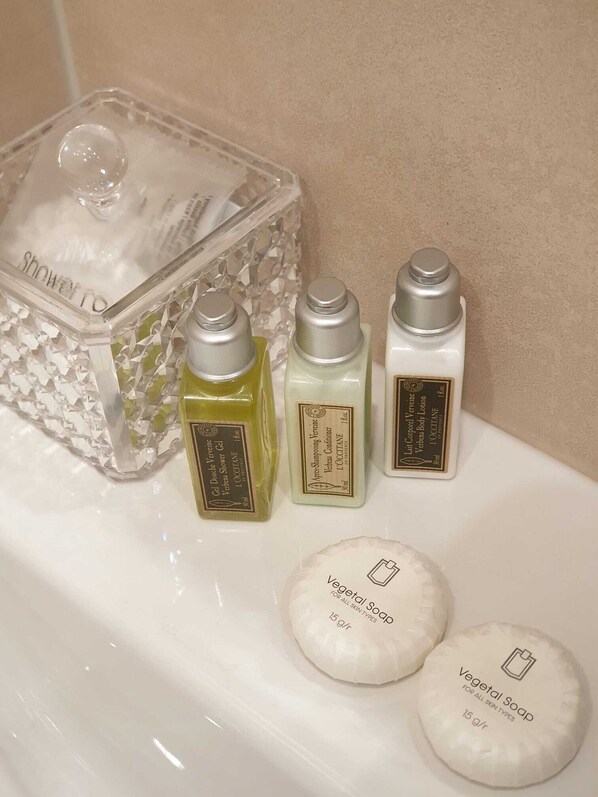 Une salle de bain avec un récipient en verre transparent contenant un flacon de lotion, deux flacons de lotion pour le corps et deux savons ronds, dont l’étiquette indique « Savon végétal ».