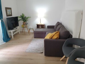 Un salon avec un canapé, un téléviseur, une lampe, une petite table et une plante.