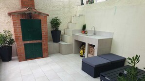 Ein kompakter Küchenbereich im Freien mit Backofen aus Ziegeln, einer Spüle und einer Sitzecke mit Kissen.