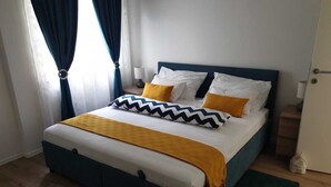 Ein ordentlich bezogenes Bett mit blauem Kopfteil, weißen und gelben Kissen sowie einer senffarbenen Decke.