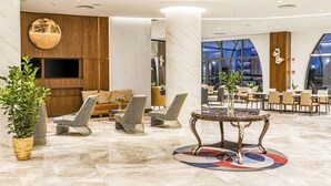 A modern lobby with a marble floor, seating area with sofas and chairs, a round table with a vase, and large windows offering a view of the cityscape. - Hilton Garden Inn Samarkand Afrosiyob (Samarkand)