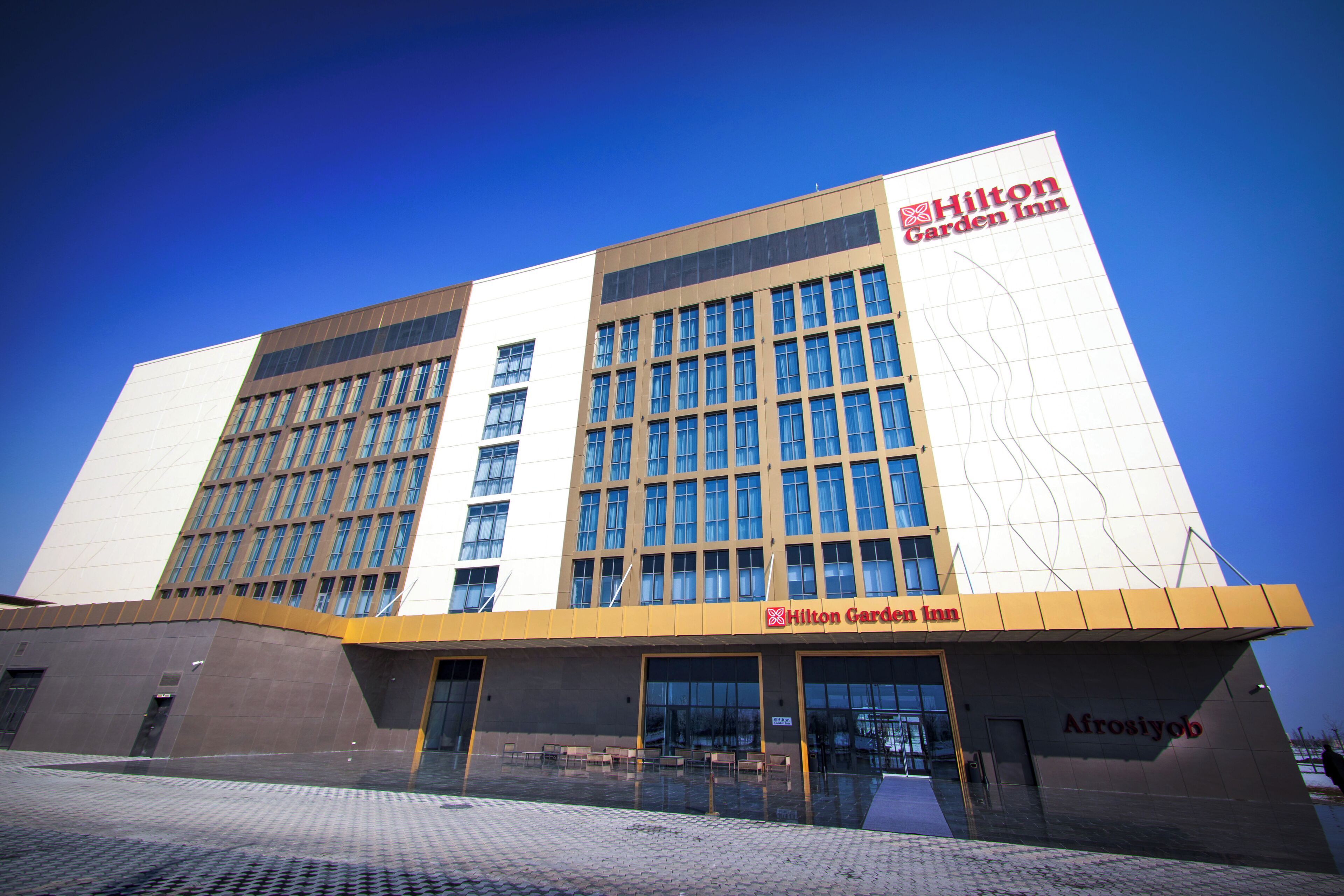A Hilton Garden Inn hotel with a modern design, featuring a large glass facade and a prominent logo on the building.