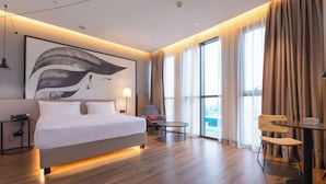 A modern hotel room with a large bed, a desk, a chair, and a large window with curtains. - Hilton Garden Inn Samarkand Afrosiyob (Samarkand)