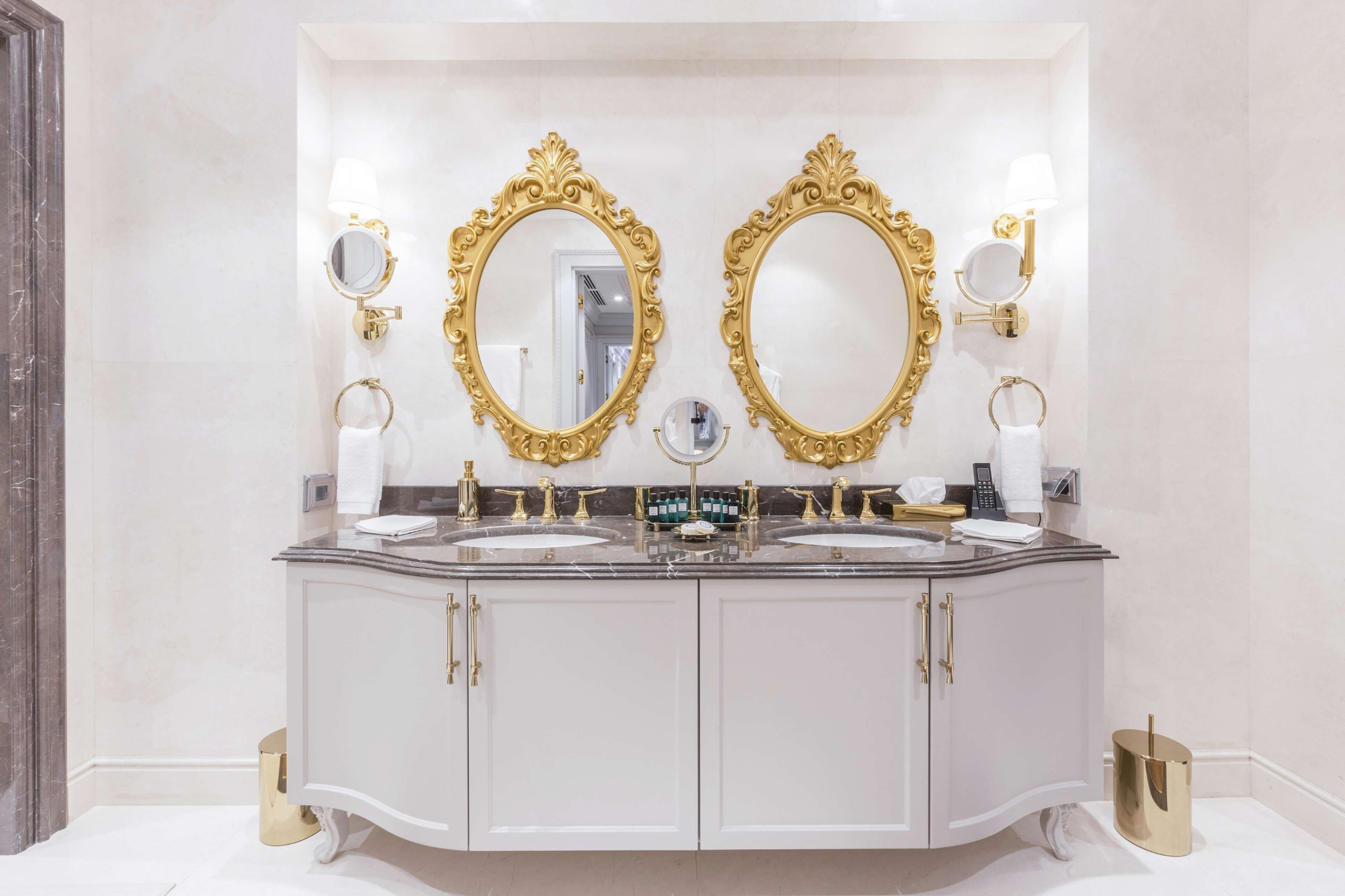 A luxurious bathroom with a double vanity, gold-framed mirrors, and a marble countertop.