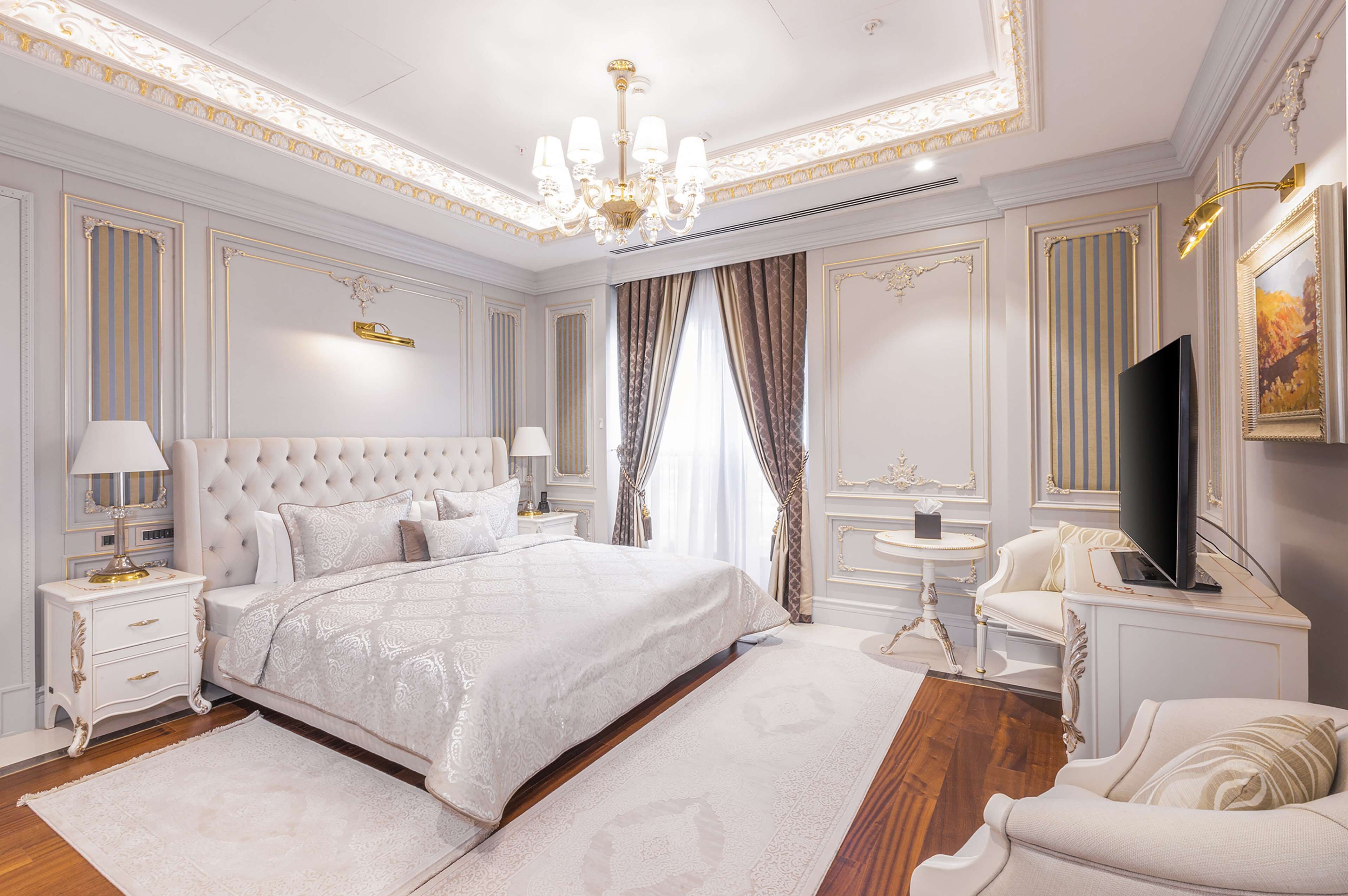 A luxurious bedroom with a large bed, a chandelier, a television, and ornate wall decorations.
