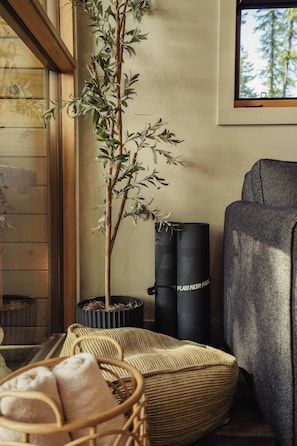 Una habitación acogedora con piso de madera, una silla tejida, una planta pequeña en maceta y una ventana con vista a árboles.