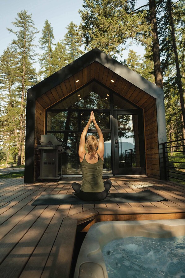 A person performing a yoga pose on a wooden deck with a hot tub in the foreground.