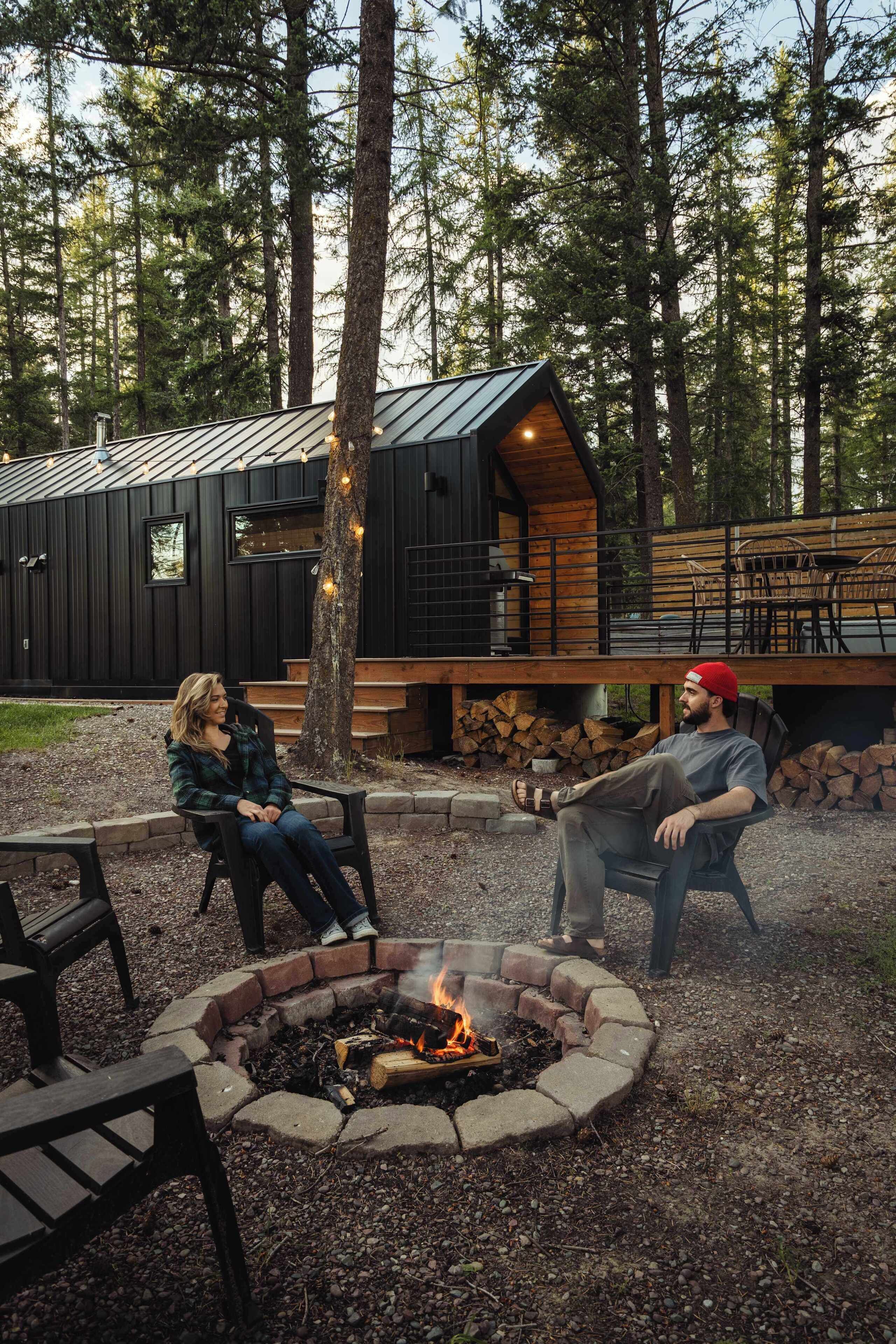 A cabin with a fire pit, outdoor seating, and a deck overlooking a forest.
