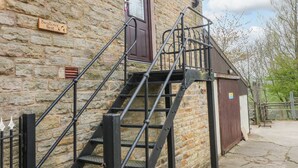 A stone building with a wooden sign reading "Swallows Nest" and a metal staircase leading to a door. - Swallows Nest (Macclesfield)