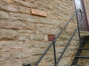 A stone wall with a wooden sign reading "Swallows Nest" and a metal staircase.