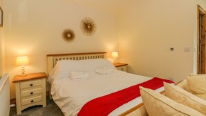 A neatly made bed with white linens and a red blanket, two bedside lamps, a wooden nightstand, and a wall-mounted decorative item. - Swallows Nest (Macclesfield)