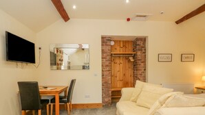 A cozy living room with a sofa, a TV, a dining table with chairs, and a brick wall. - Swallows Nest (Macclesfield)