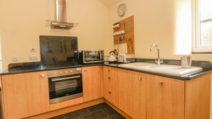 A compact kitchen with wooden cabinets, a stove, a microwave, a toaster, and a sink. - Swallows Nest (Macclesfield)
