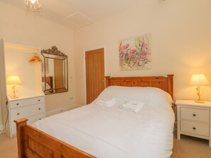 A neatly made bed with white linens, a wooden headboard, and a painting of flowers on the wall.