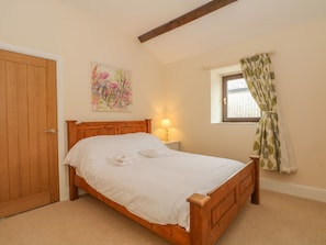 Une chambre à coucher avec un lit en bois, une table de chevet avec une lampe, une fenêtre avec des rideaux et une porte.