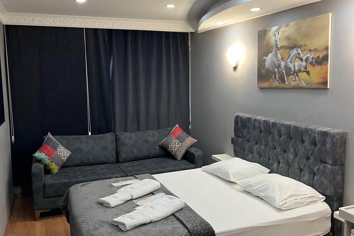 A modern bedroom with a large bed, grey upholstered sofa, and a painting of horses.