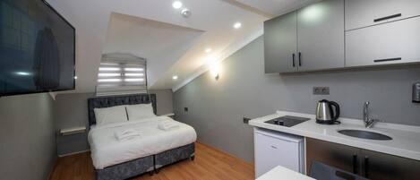 A modern bedroom with a bed, a small kitchenette, and a TV mounted on the wall.