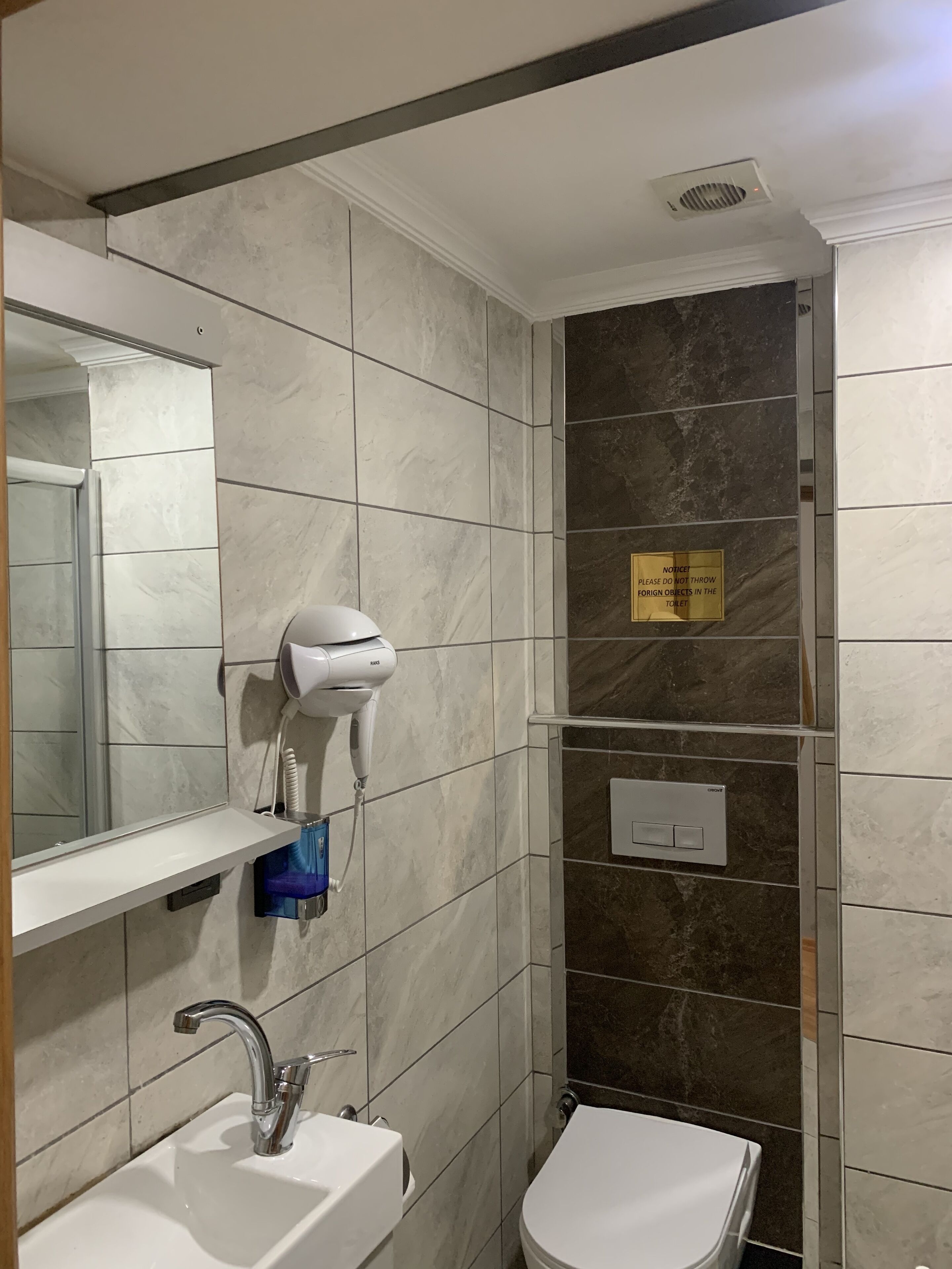 A bathroom with a sink, mirror, hairdryer, and a sign on the wall.