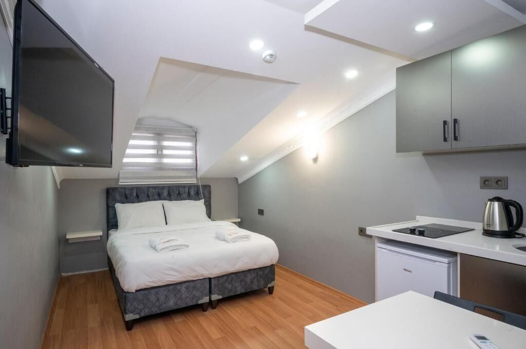 A modern bedroom with a bed, a flat-screen TV, a kitchenette, and a ceiling light.