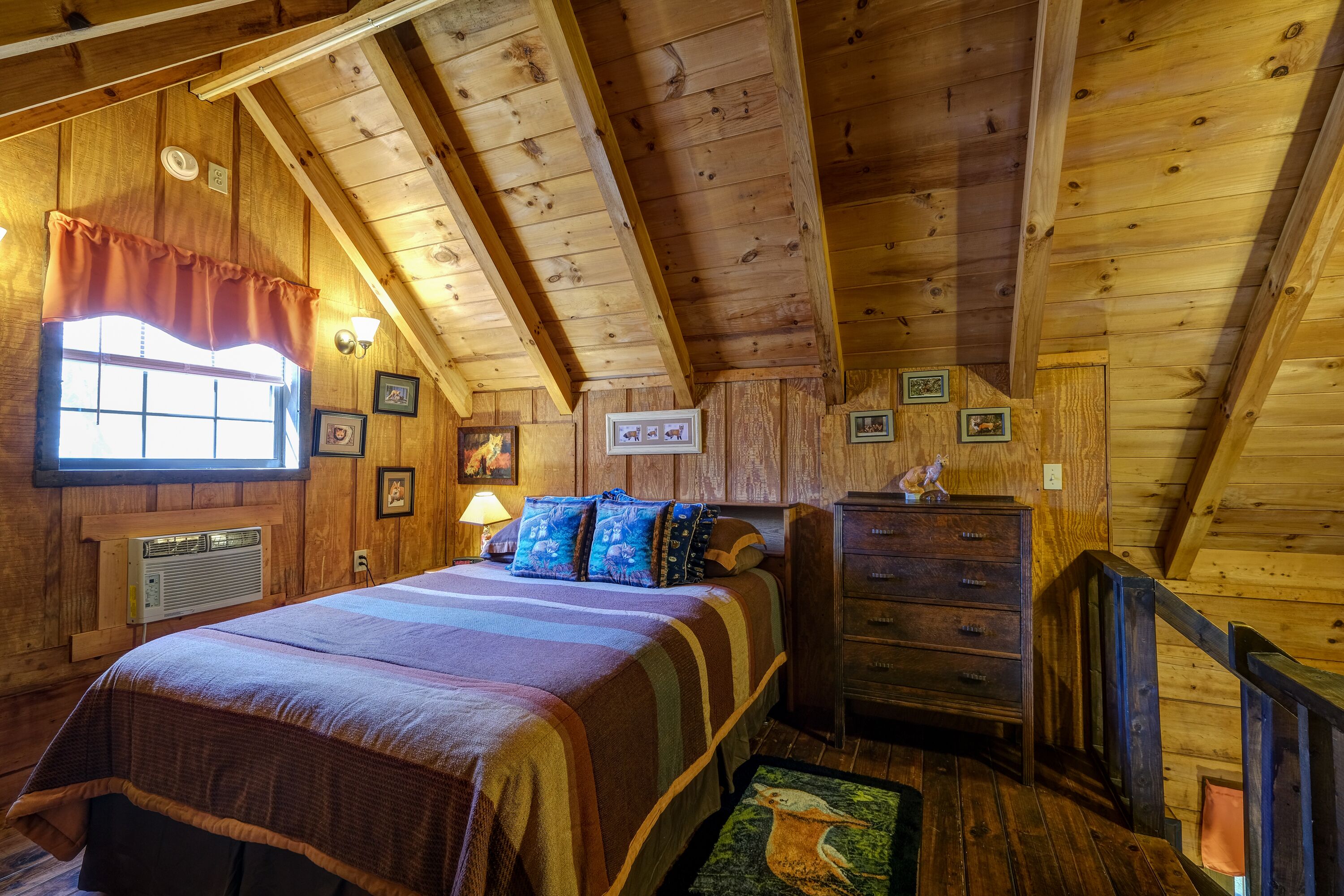Ein gemütliches Schlafzimmer einer Holzblockhütte mit Bett, Schminktisch und einem fenster mit Vorhängen.
