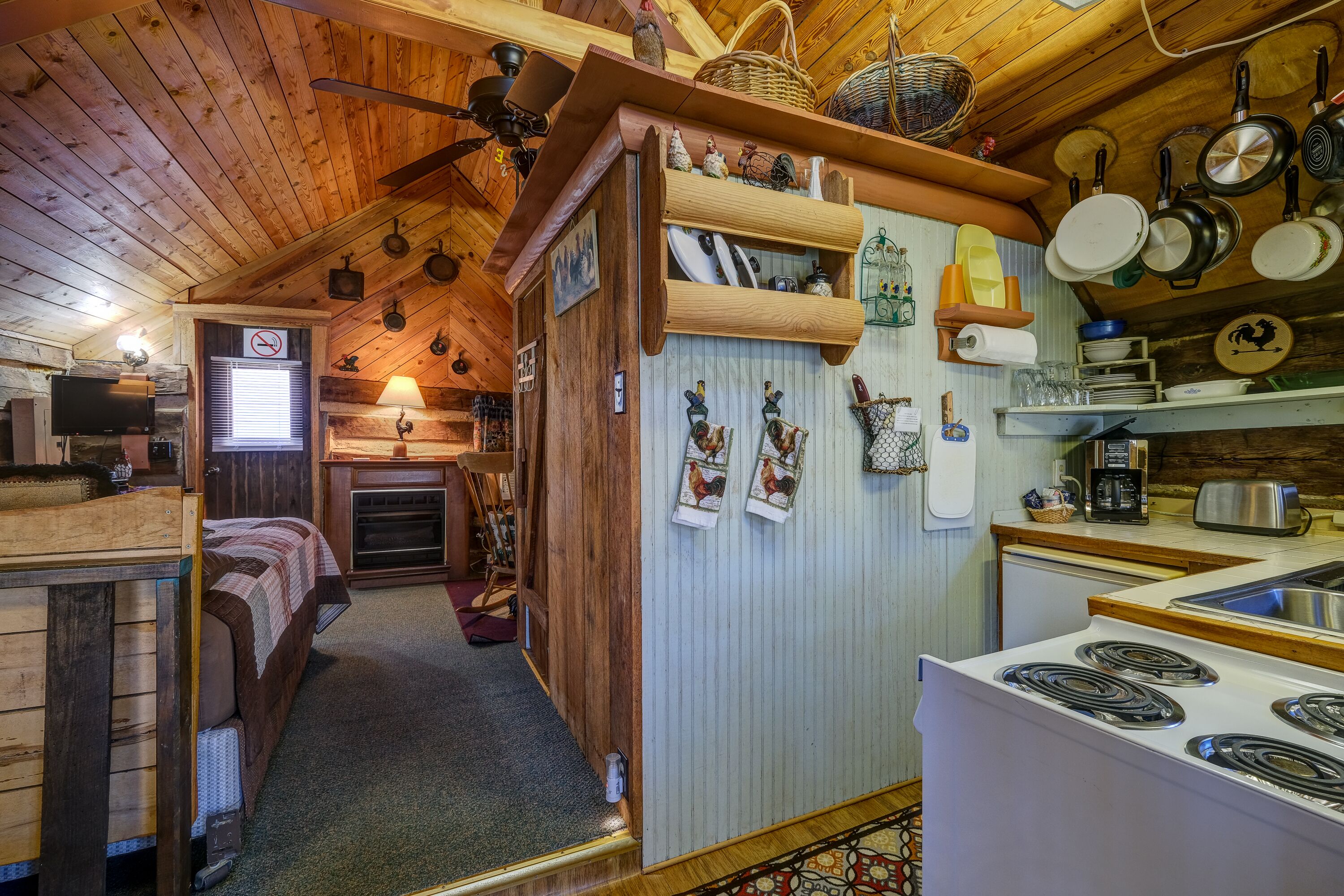 Interior acogedor de una cabaña con techo de madera, chimenea, comedor con estufa y cocina con ollas colgantes.