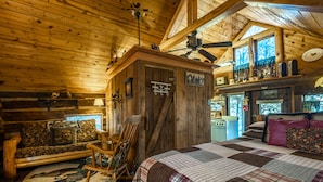 Interior acogedor de una cabaña de madera con techo de madera, una mecedora, cama acolchada y una zona de cocina rústica.