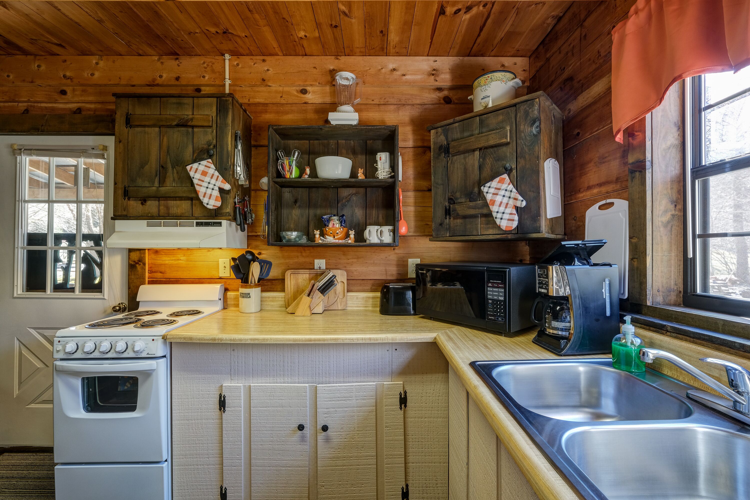 A kitchen with wooden cabinets, a stove, a microwave, and a sink.