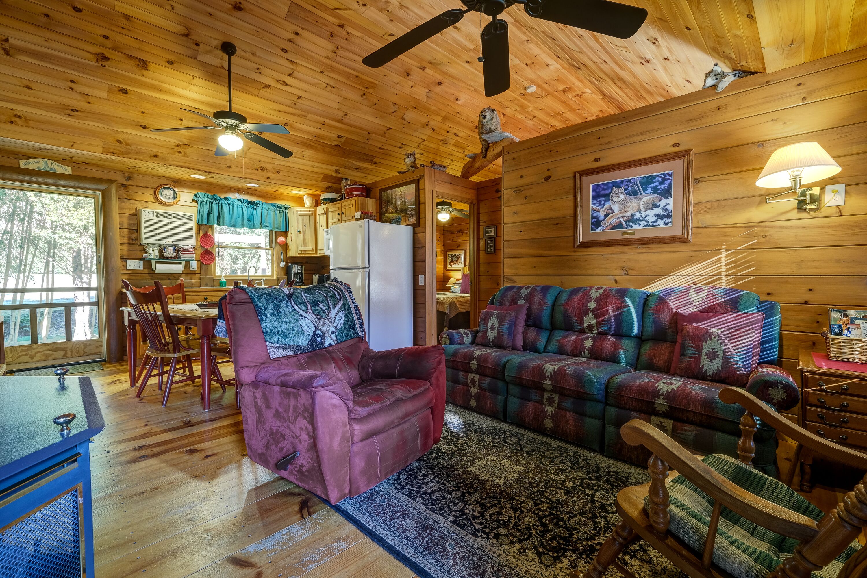 L’intérieur chaleureux d’un chalet avec des murs en bois, un coin repas, un salon doté d’un canapé et de fauteuils, et un ventilateur de plafond.
