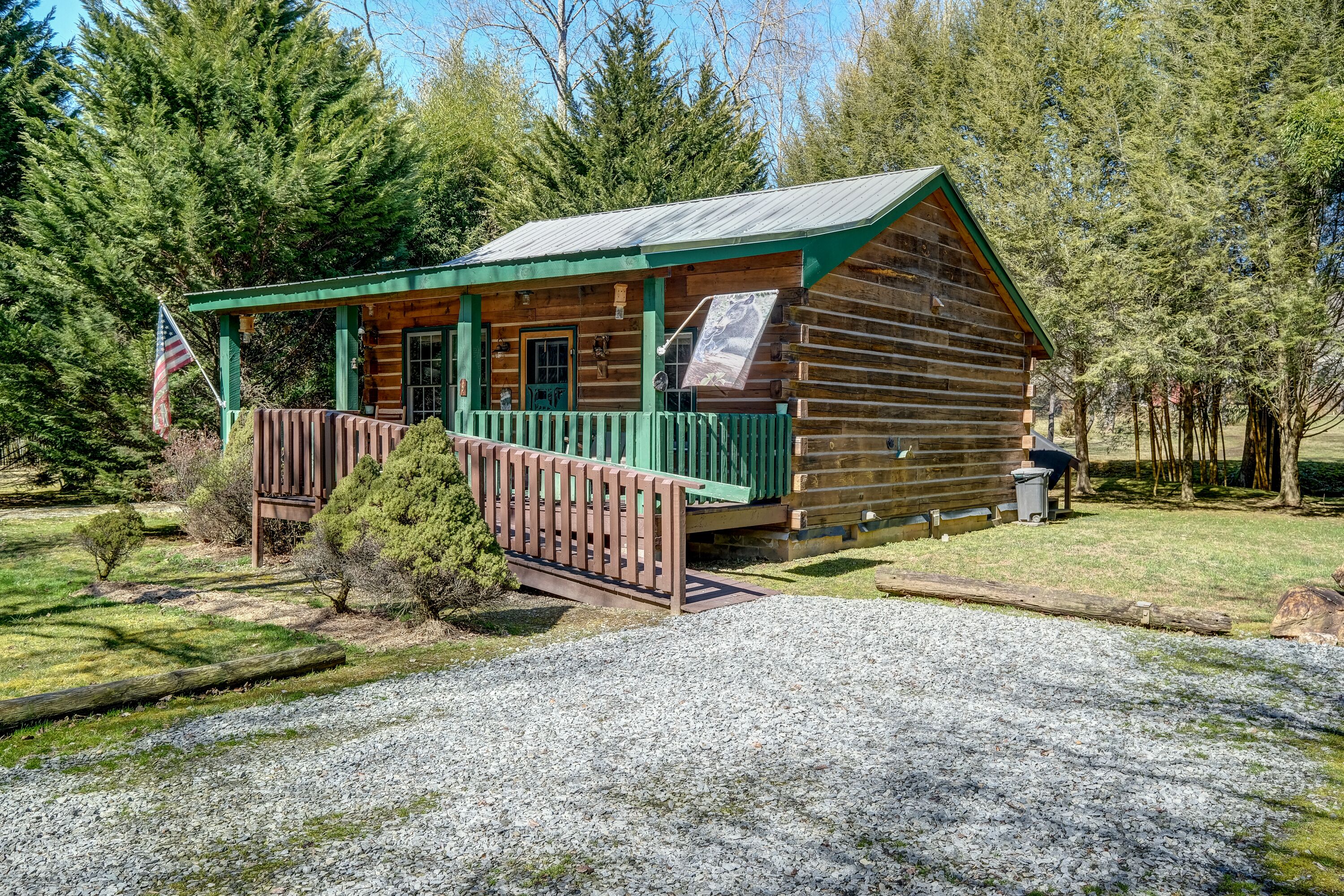 Una baita di legno con un portico verde e un piccolo patio, immersa tra gli alberi.