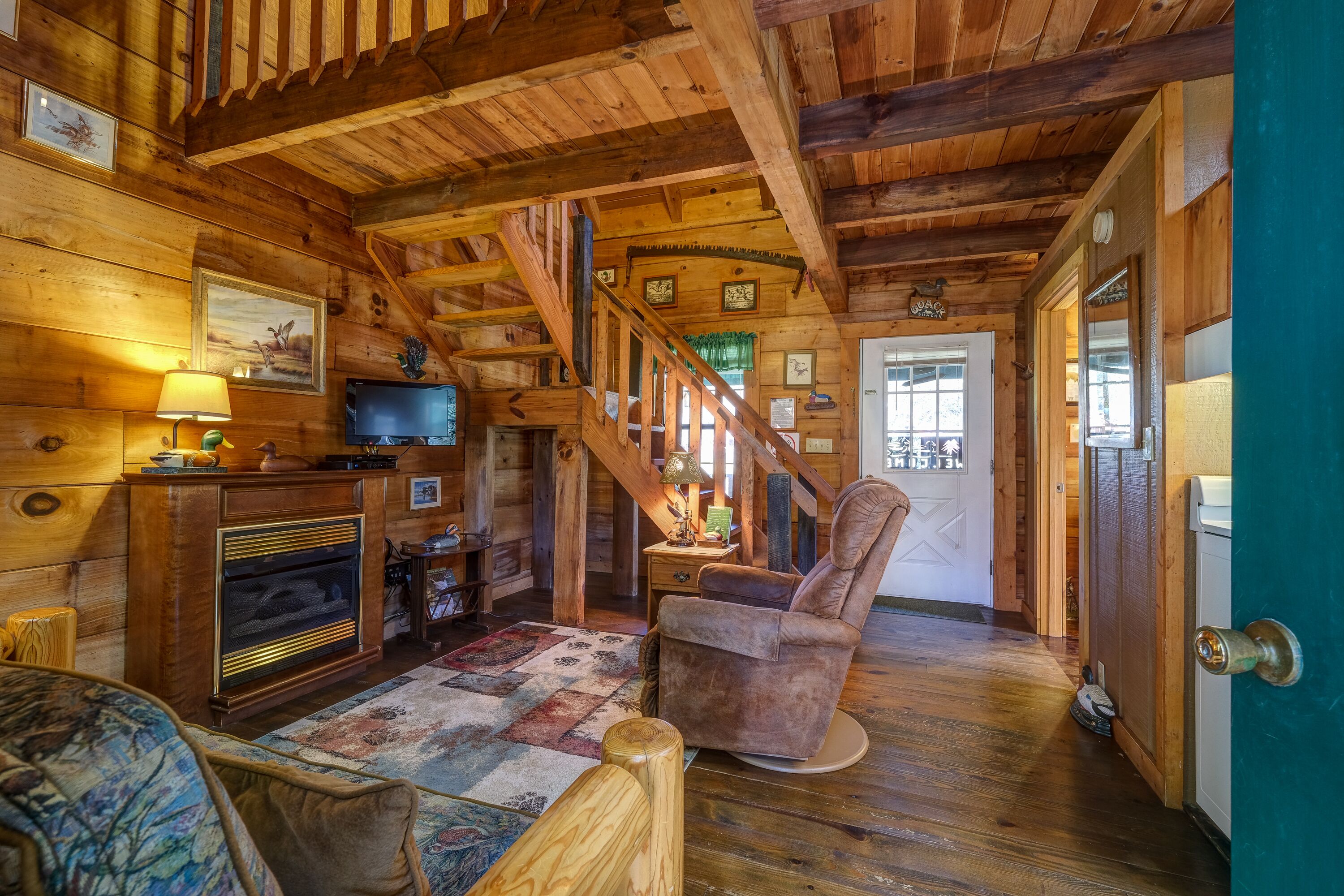 A cozy cabin interior with wooden walls, a fireplace, a television, and a comfortable chair.