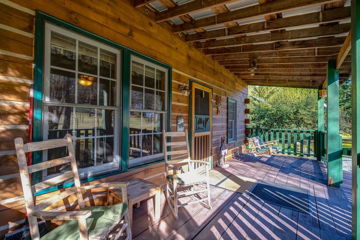 A wooden cabin with a porch, large windows, and a green railing.
