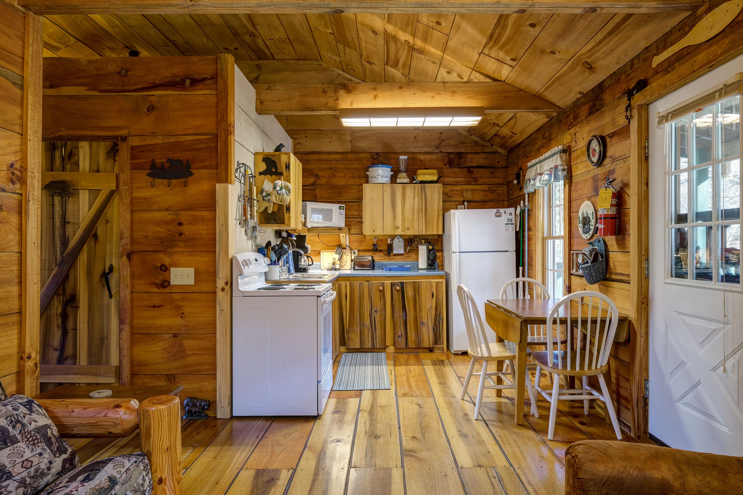 A wooden cabin interior with a kitchen, dining area, and a cozy seating space.