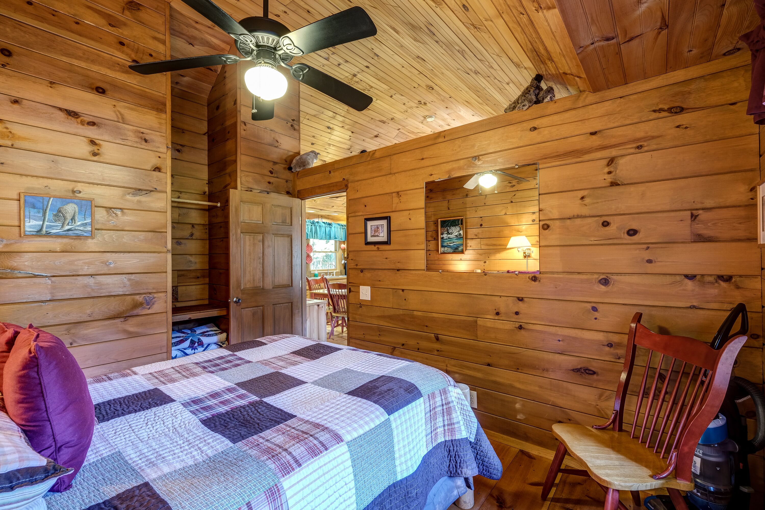 Ein Holzblockhaus-Interieur mit einem Bett, einem Sessel, einem Deckenventilator und einem Kamin.