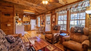 Interior acogedor de una cabaña con paredes de madera, una zona de comedor y un espacio de estar con chimenea.
