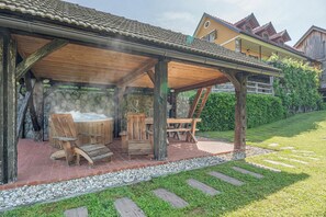 A covered outdoor seating area with a hot tub, wooden furniture, and a stone wall backdrop. - Traditional House Kal Garden & Jacuzzi (Semič)