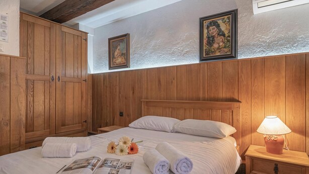 A bedroom with a wooden headboard, a bed with white linens, a nightstand with a lamp, and two framed pictures on the wall. - Traditional House Kal Garden & Jacuzzi (Semič)