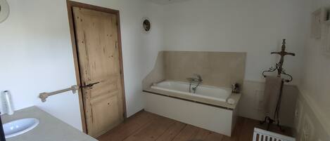 A bathroom with a wooden door, a bathtub, a sink, and a bench.