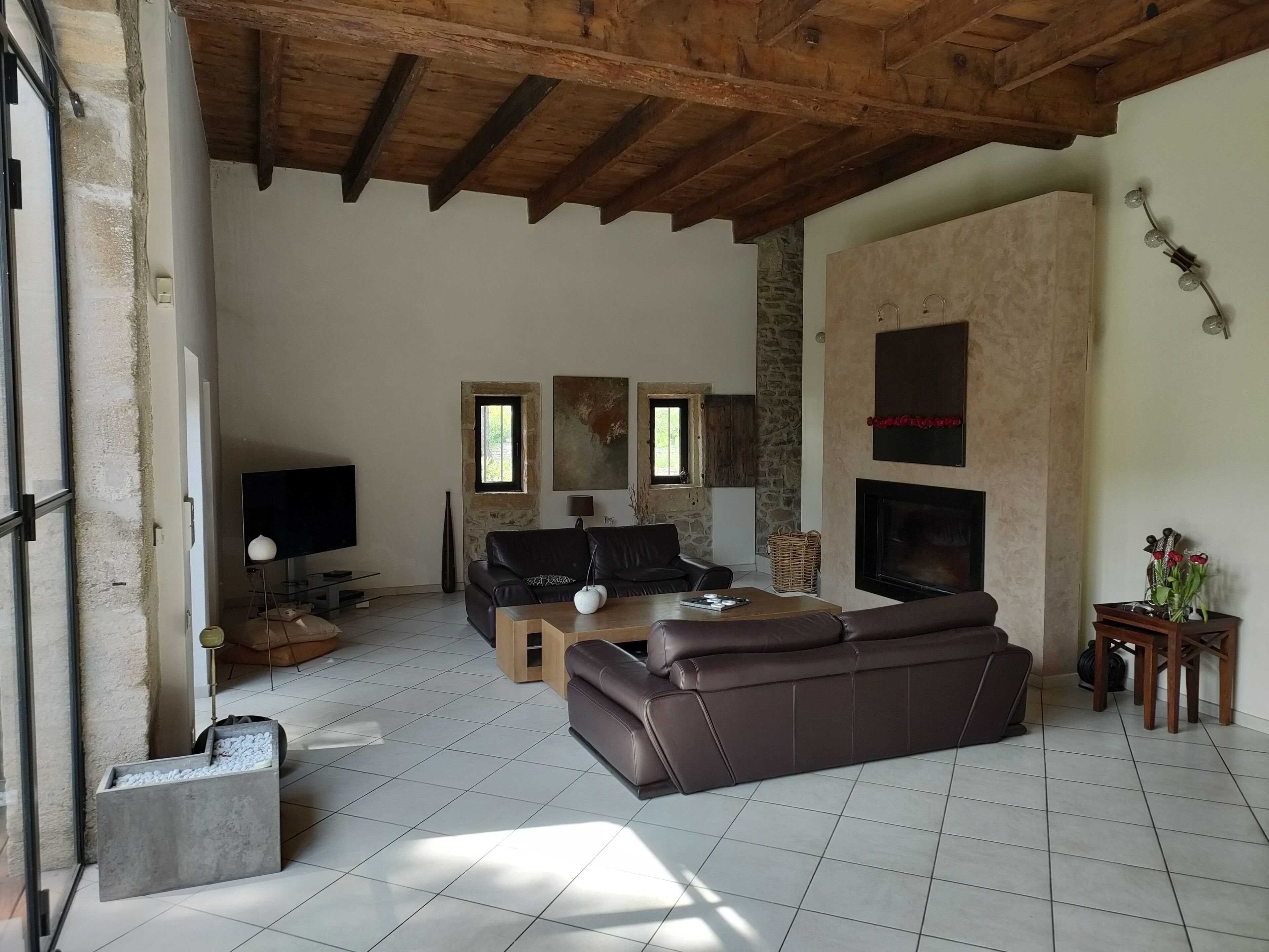 Amplia sala de estar con un sofá de cuero marrón, televisor de pantalla plana, chimenea y pared de piedra.