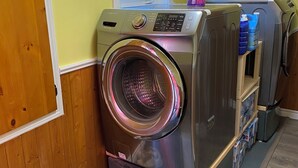 Une buanderie équipée d’un lave-linge et d’un sèche-linge à chargement frontal, de lambris en bois, d’une fenêtre et d’un porte-chaussures avec des chaussures.