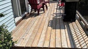 Une terrasse en bois avec des chaises Adirondack rouges et un barbecue, donnant sur une étendue d’eau.