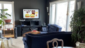 Un salon avec un canapé de couleur sombre, une table à manger en bois et un téléviseur à écran plat fixé au mur.