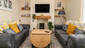 En stue med to grå sofaer, et træbord, et fladskærms-tv ophængt på væggen og en pejs.
