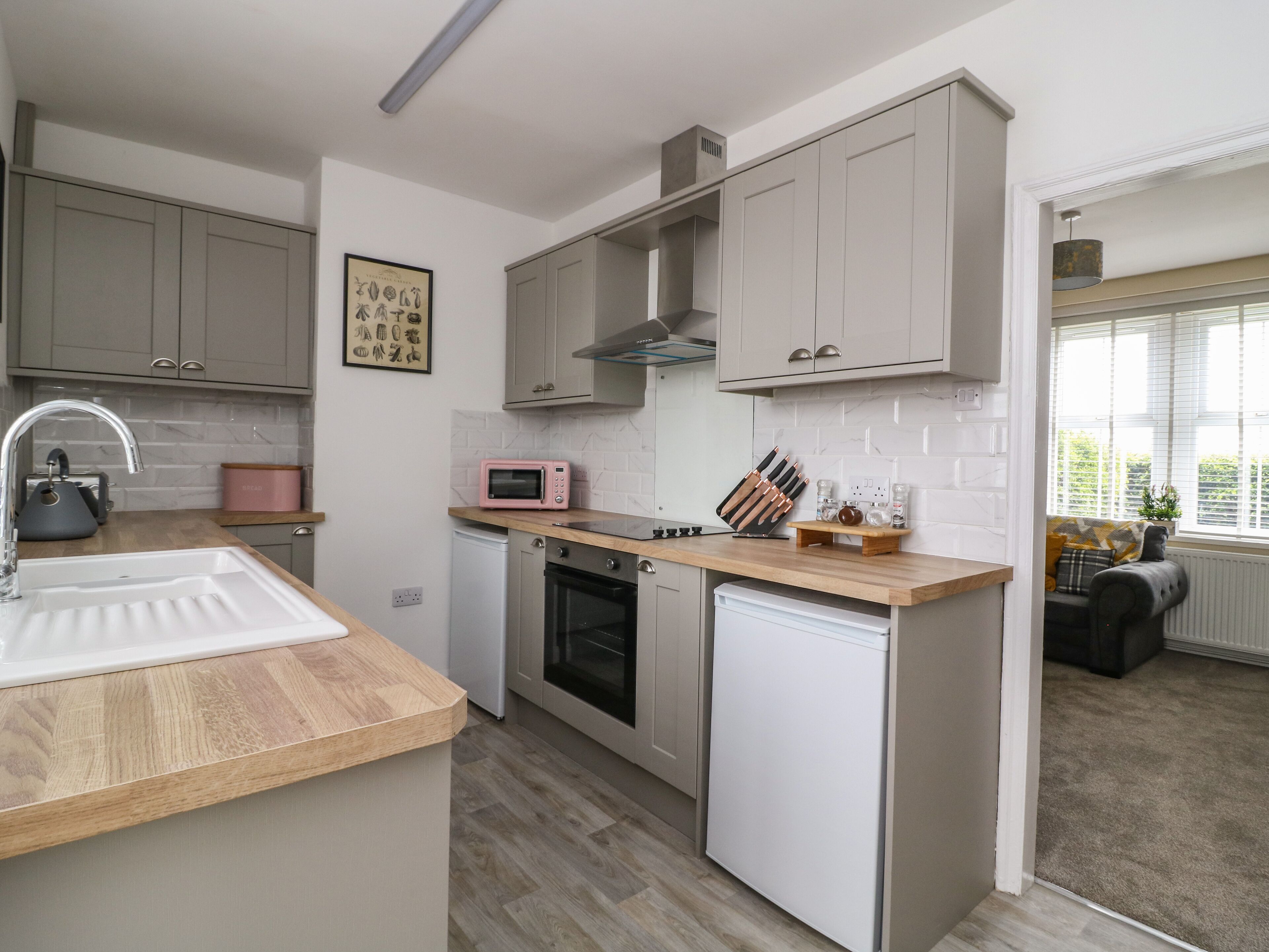 A modern kitchen with grey cabinets, a wooden countertop, a sink, a microwave, and a dishwasher.