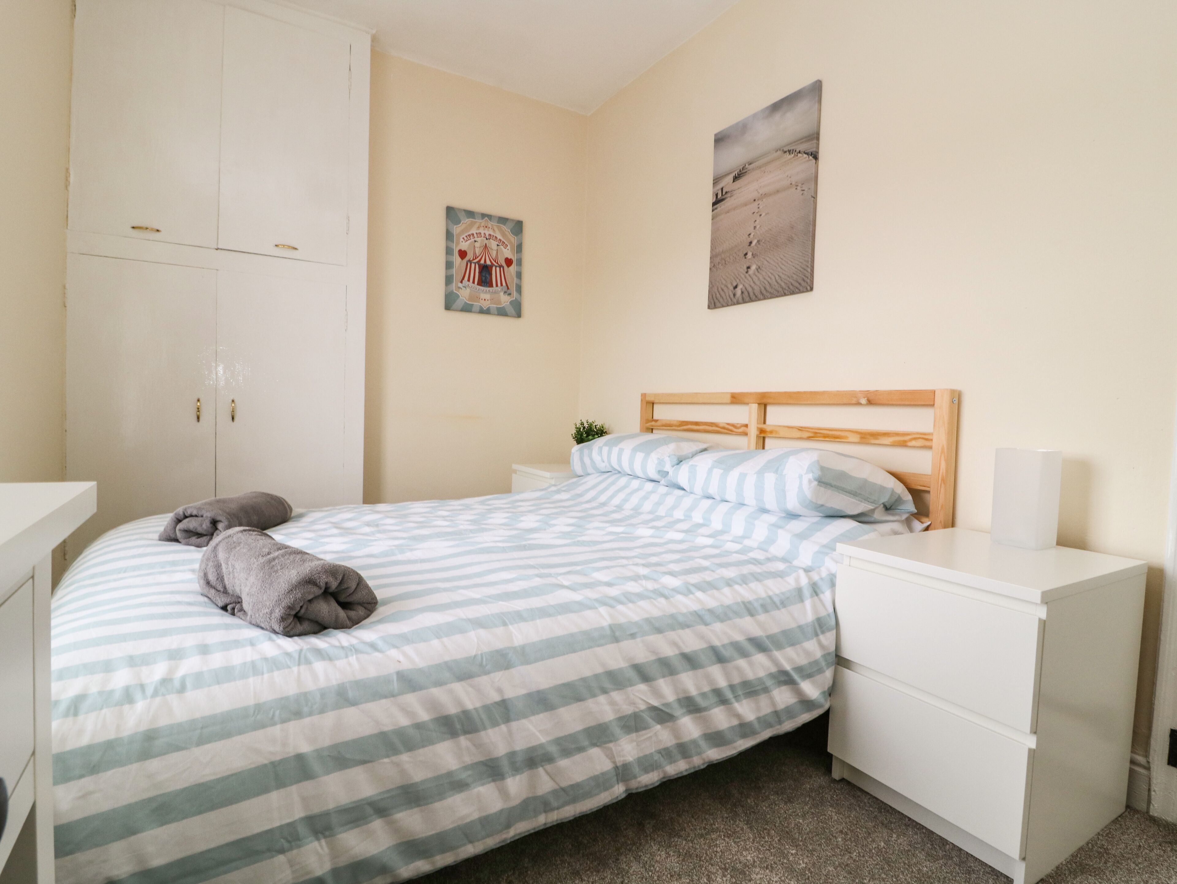 Een slaapkamer met een bed, nachtkastje, kledingkast en een muur met een schilderij.