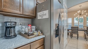 A kitchen with a refrigerator, coffee maker, and a sign that says "But First Coffee". - Elegant Art Deco Home designed with you in mind (El Paso)
