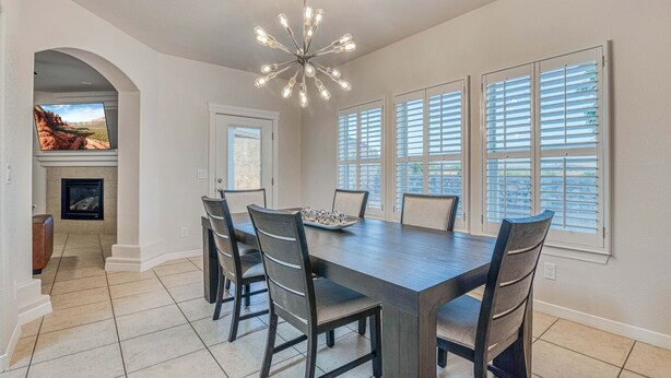 A dining room with a large table, chairs, a chandelier, and large windows with blinds. - Elegant Art Deco Home designed with you in mind (El Paso)