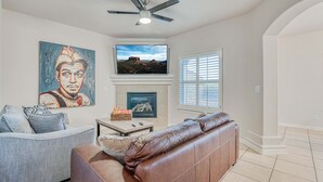 A living room with a fireplace, a television, and a ceiling fan. - Elegant Art Deco Home designed with you in mind (El Paso)
